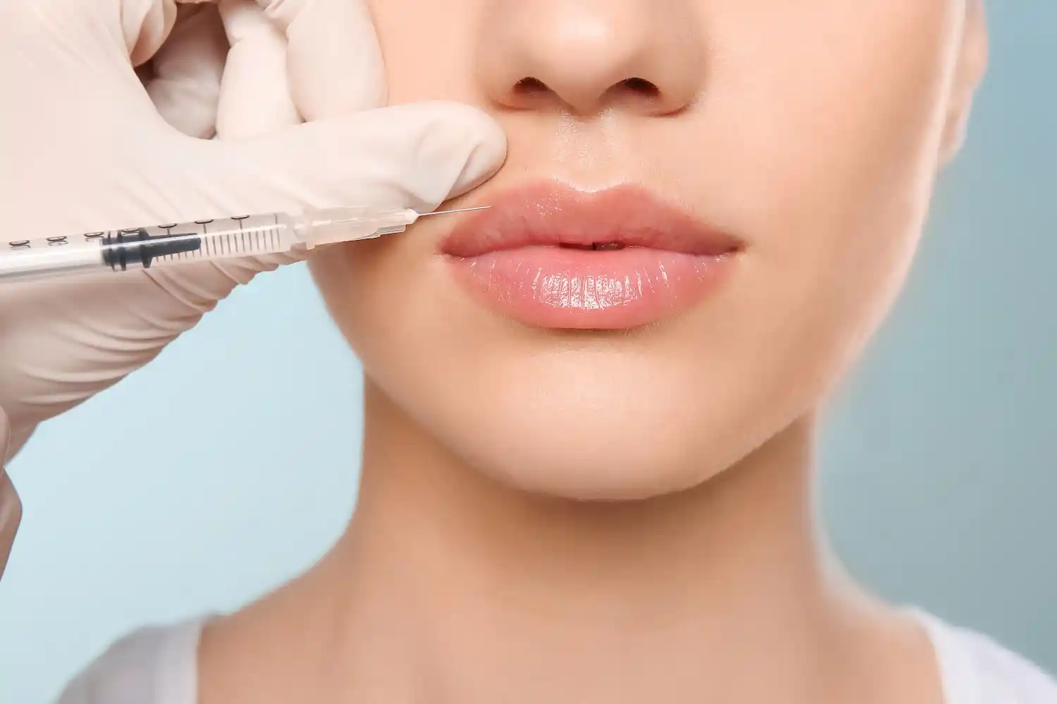 Close-up of a person’s lips as a gloved hand holds a syringe with a needle positioned at the upper lip.