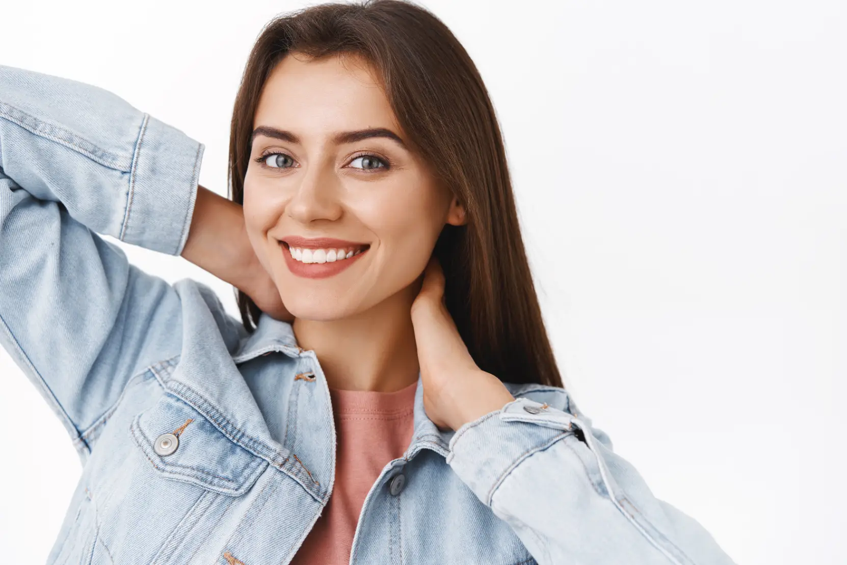 Smiling woman in denim jacket posing with hands near jawline and neck
