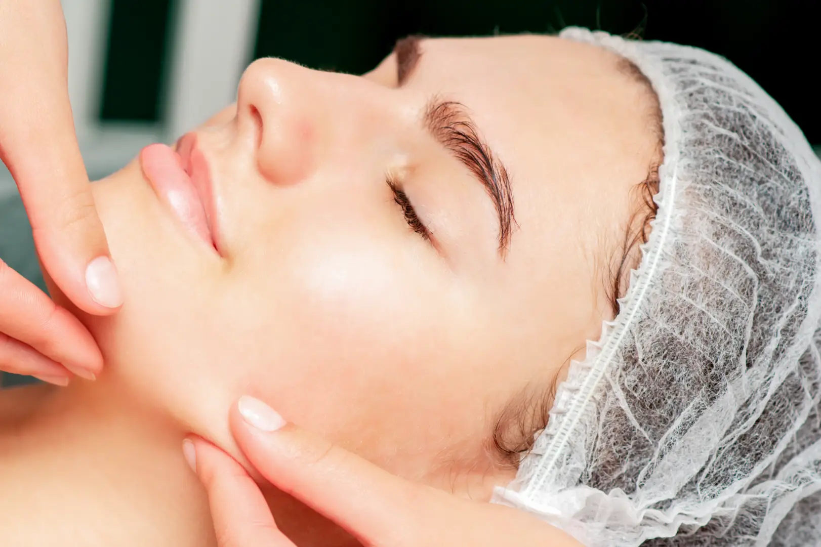 Woman with hair cover receiving facial treatment on cheeks and jawline