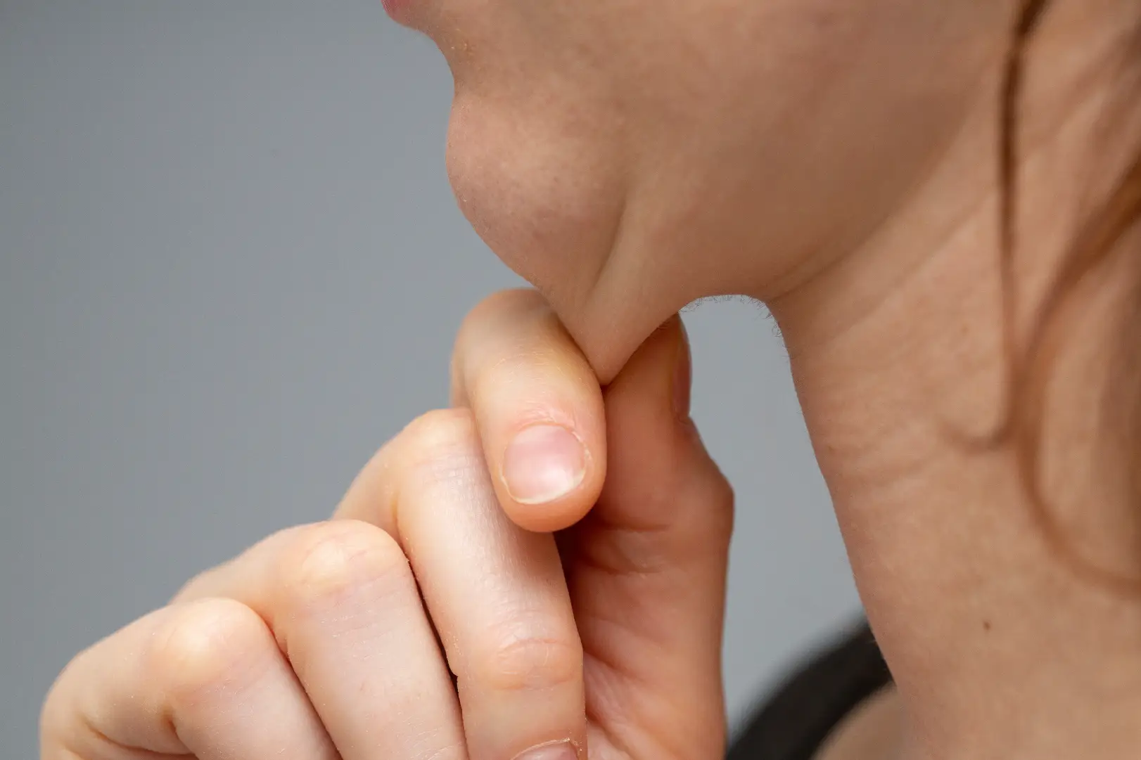 Close-up of a hand gently pinching skin beneath the chin from a side angle.