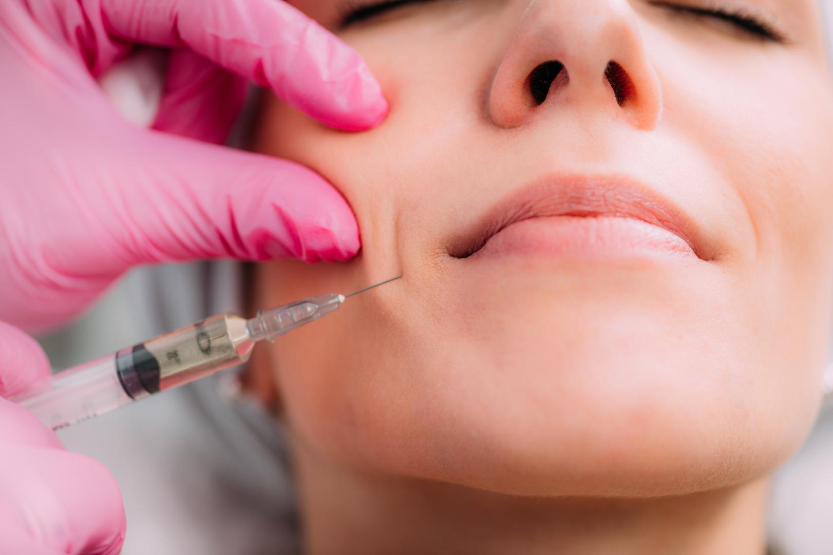 Practitioner holding facial skin while positioning a syringe near the lower cheek and jawline.