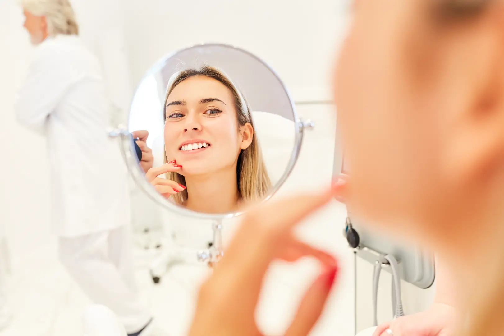 Woman looks at her reflection in a round mirror while touching her chin with one finger.