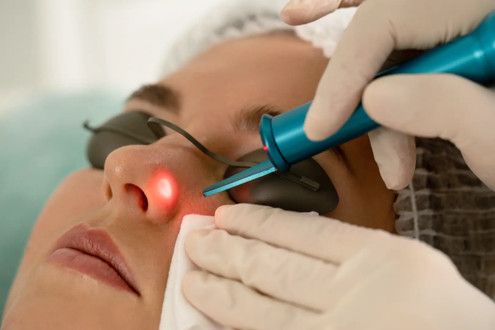 Practitioner holds a handheld device near a woman's cheek as she wears protective eye covers.